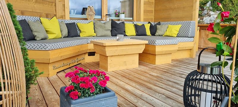 Terrasse mit Holzsitzbank mit hellgrauer Polsterung und Kissen in Gelb und Anthrazit von Raumdesign Stefanie 02