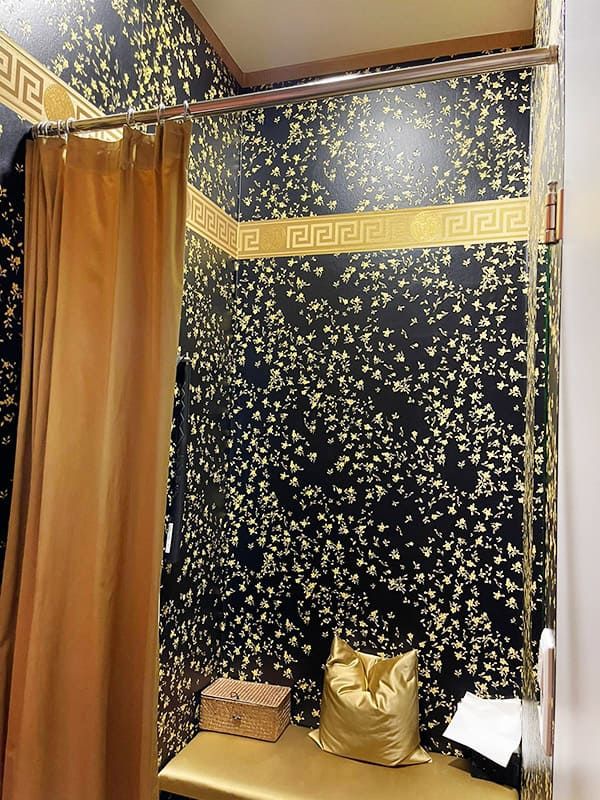 Umkleidekabine in einer Arztpraxis, tapeziert mit einer schwarz-goldenen Tapete von Versace