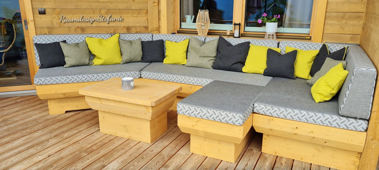 Terrasse mit Holzsitzbank mit hellgrauer Polsterung und Kissen in Gelb und Anthrazit von Raumdesign Stefanie 02